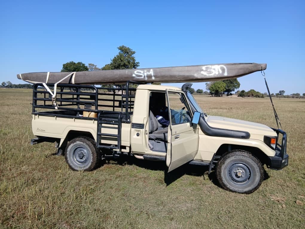 4x4 safari vehicle carrying a mokoro canoe on its roof rack across the grasslands en route to Samonyana