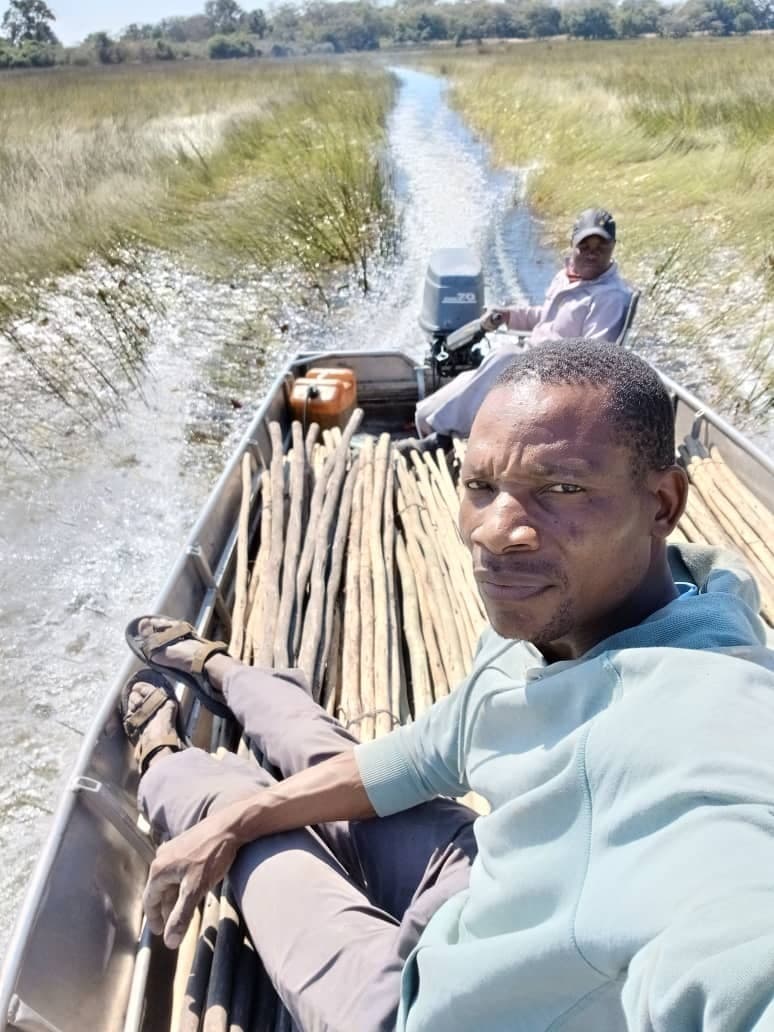 Staff travelling by motorboat through a narrow reed-lined channel in the Okavango Delta with supplies loaded aboard.