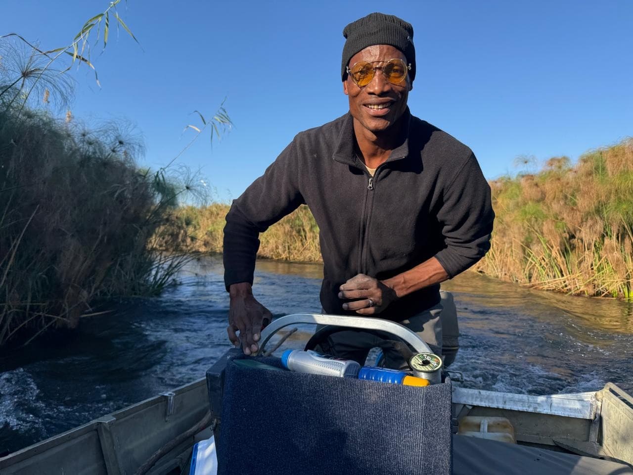 Guide smiling while steering a boat through a reed-lined channel in the Okavango Delta