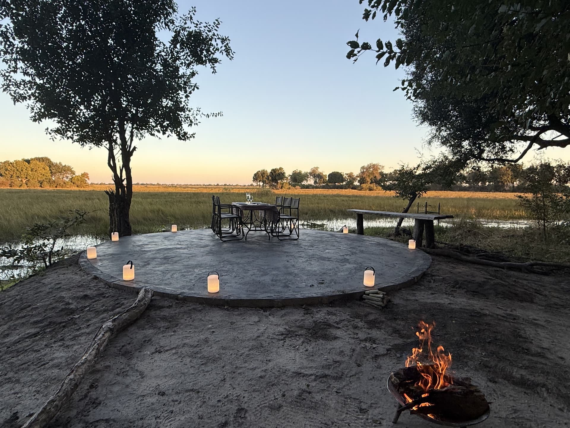 Candlelit boma dining setup with a glowing fire pit overlooking the floodplain at dusk at Samonyana Private Island.