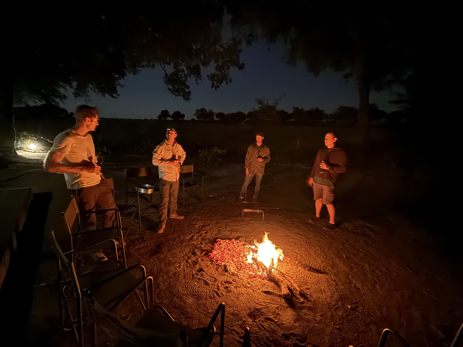 Guests standing around a crackling campfire at night under a starlit sky at Samonyana