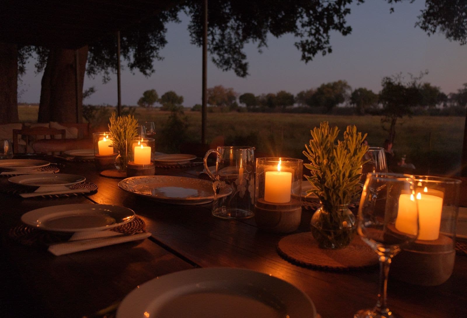 Candlelit dining table set for guests overlooking the floodplain at dusk at Samonyana Private Island.