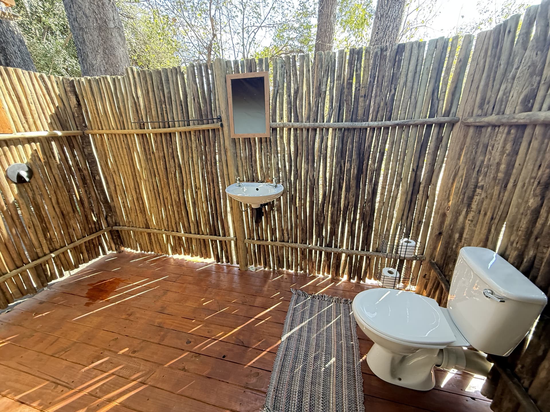 Open-air en-suite bathroom with reed privacy walls and a wooden deck floor at Samonyana Private Island.