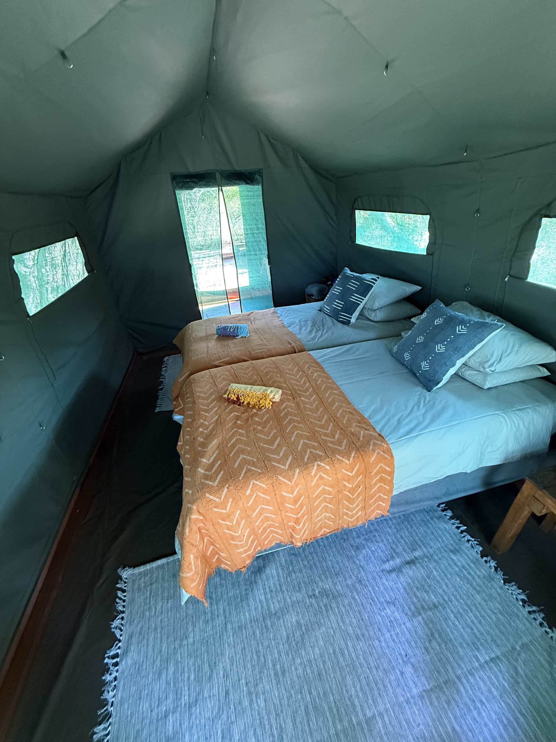 Interior of a safari tent bedroom with twin beds dressed in orange African-print throws at Samonyana Private Island.
