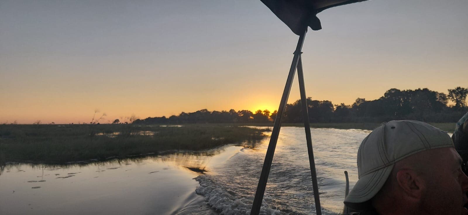 Guide steering a boat along an Okavango Delta channel as the sun sets near Samonyana