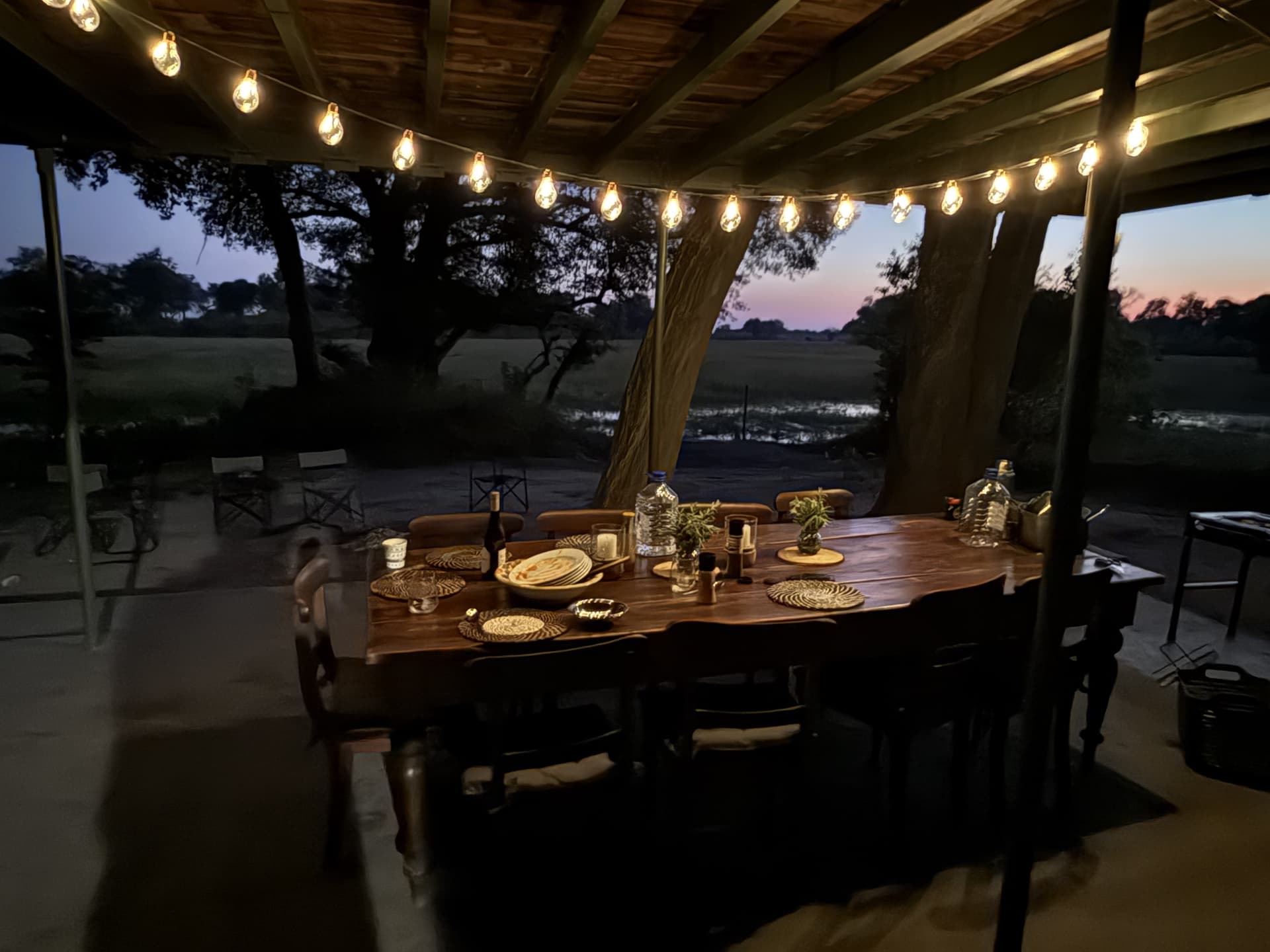 Outdoor dining table strung with fairy lights overlooking the floodplain at dusk at Samonyana.